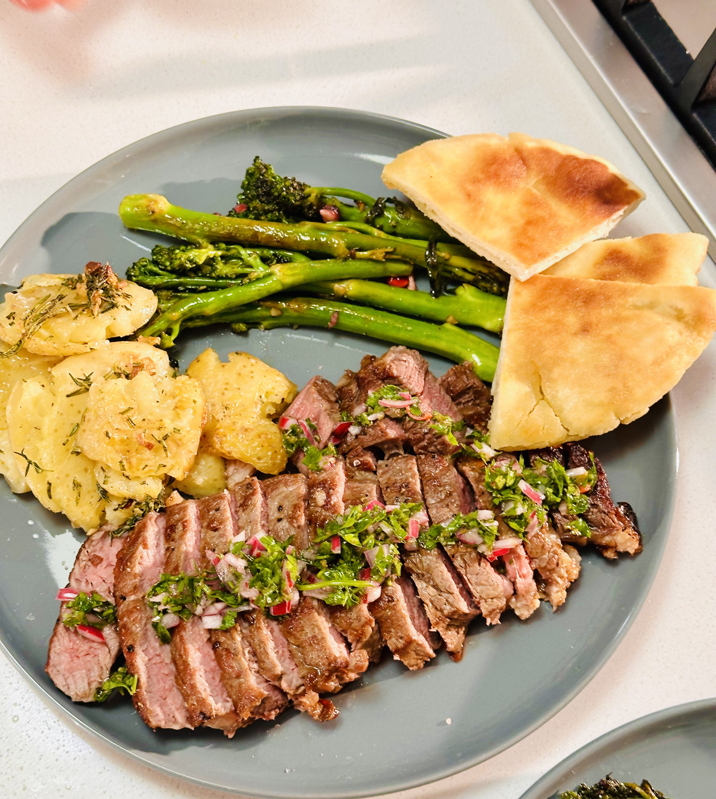 A plated meal of sliced steak, broccolini and smashed potato